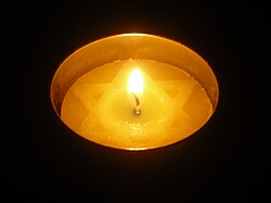 Lit yahrzeit candle glowing against a black background